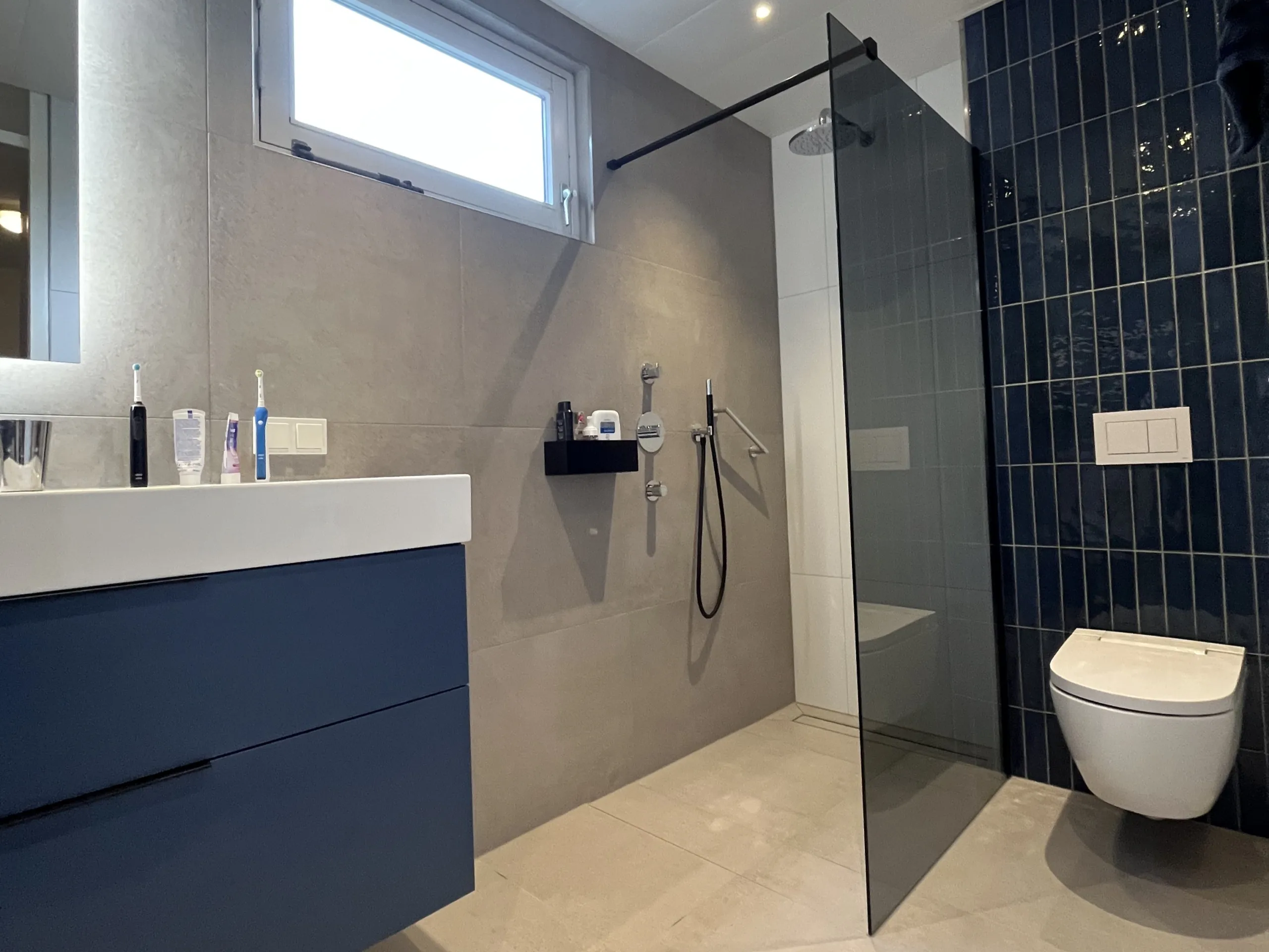 Na de renovatie – Badkamer met blauwe accenten en inloopdouche met grijs rookglas
