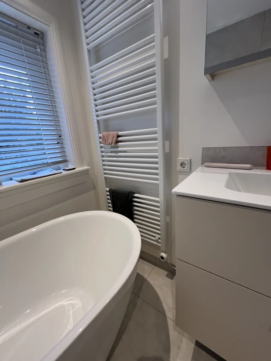 Vrijstaand bad naast handdoekradiator en badmeubel